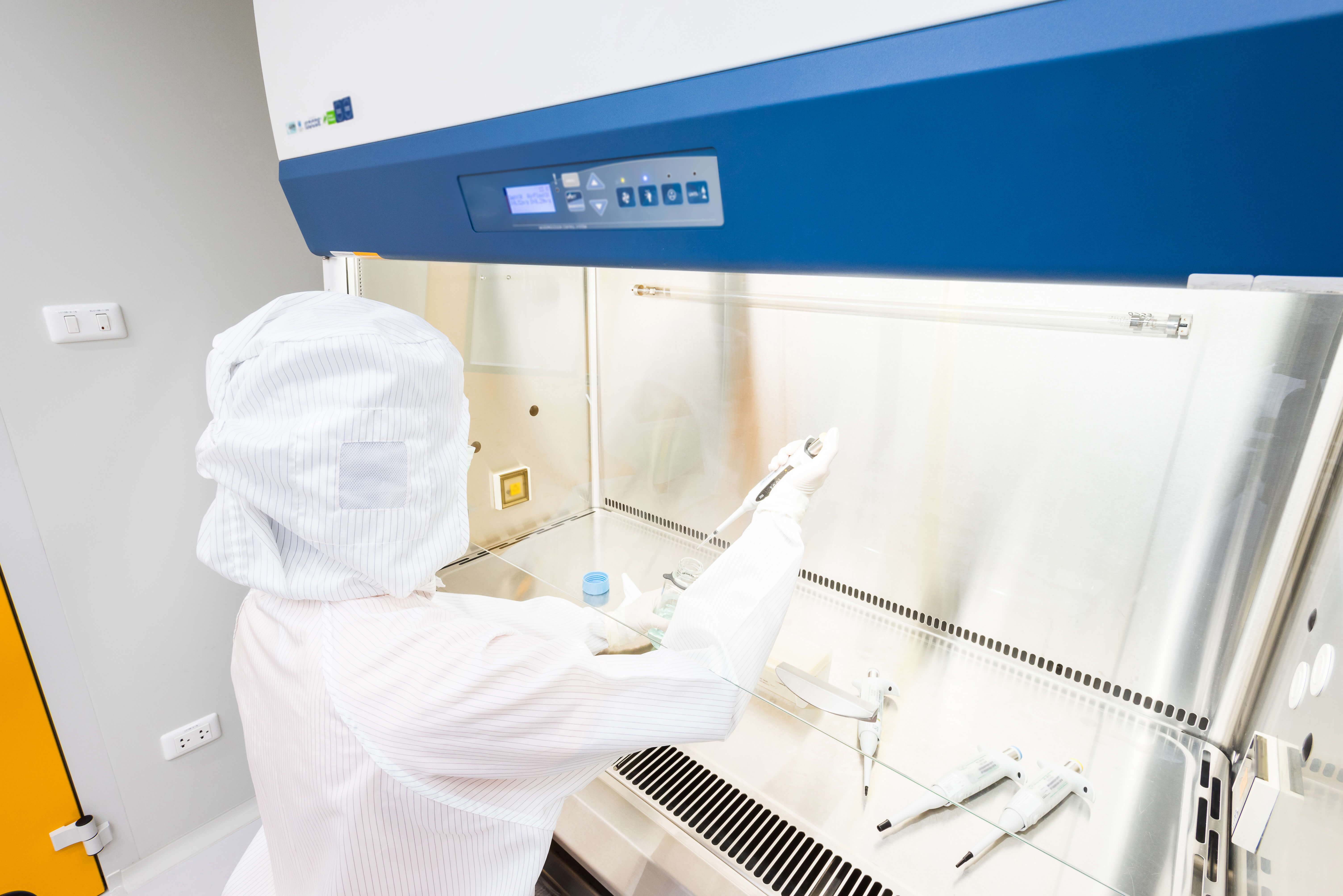 EHS Analytical Solutions, Inc - A scientist in sterile coverall gown pipetting medium or reagents for cell culture experiment in biological safety cabinet. Doing biological research in clean environmental. Cleanroom facility